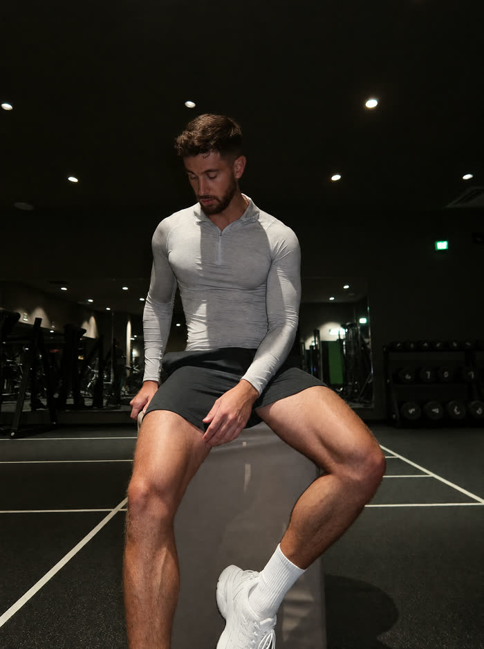 Man in a grey quarter-zip sitting on a plyo box