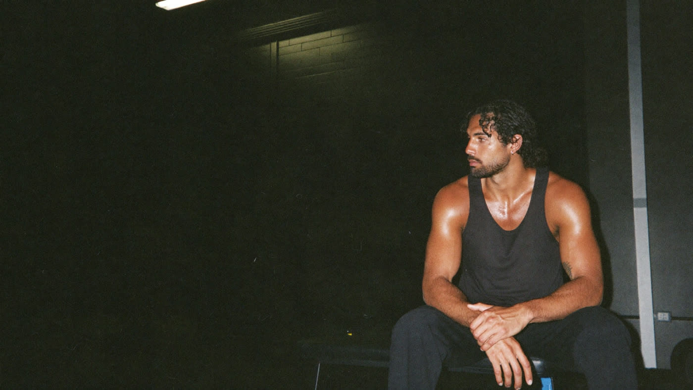 Man resting on a bench between sets in a black tank and joggers